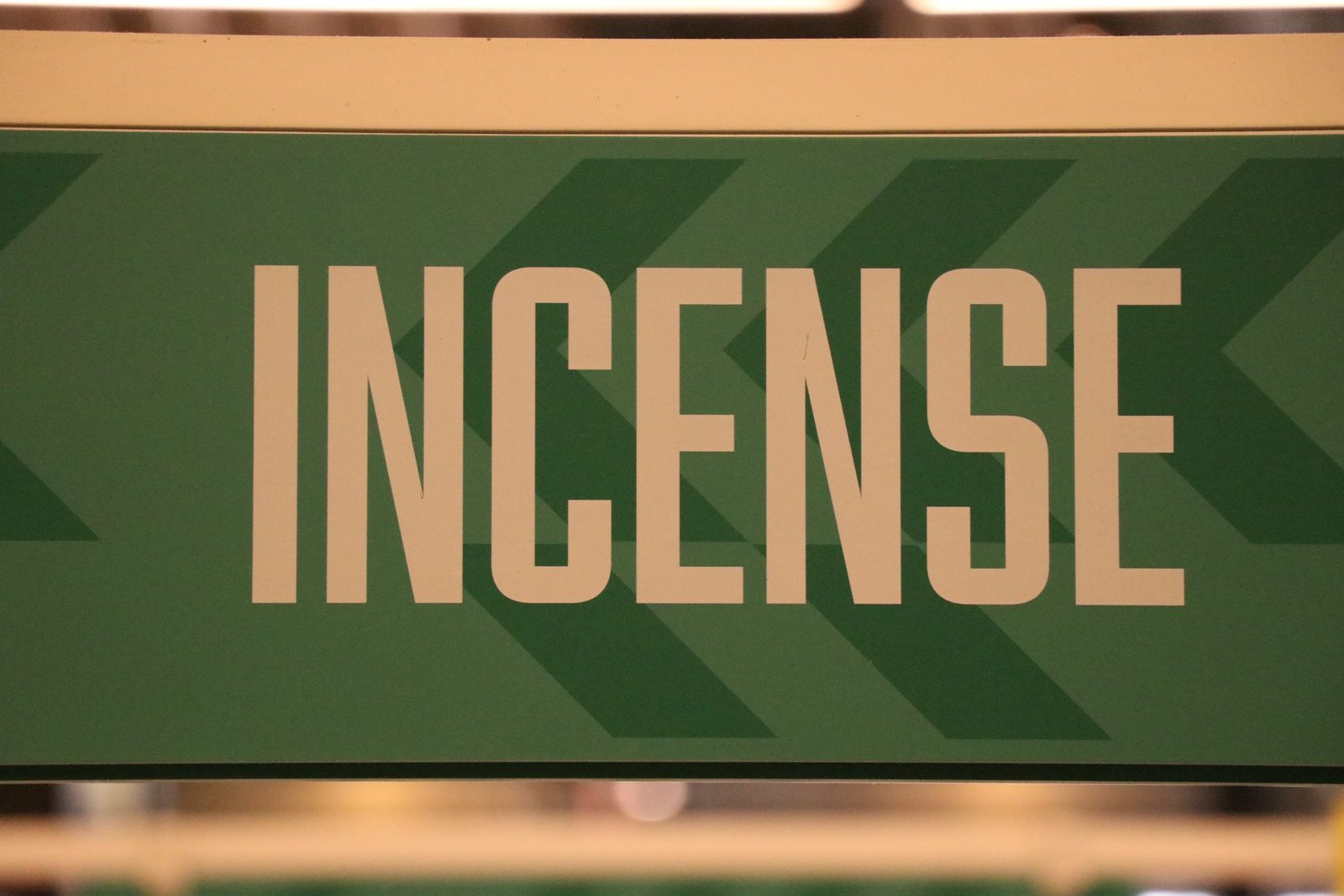 A green shop sign with the word INCENSE in tall cream letters.