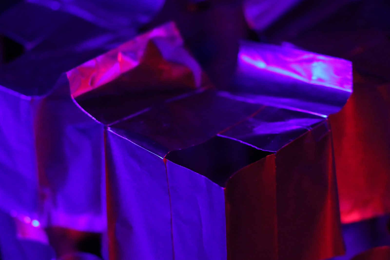 Close view of a folded paper cube lit in red and violet.