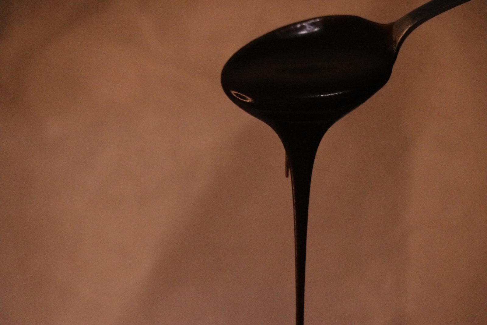 Melted chocolate dripping from a spoon against a warm brown background.