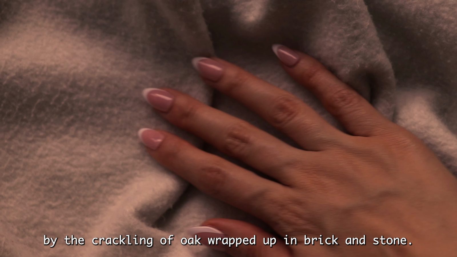 Film still: a hand resting on a soft blanket with a subtitle from the poem.